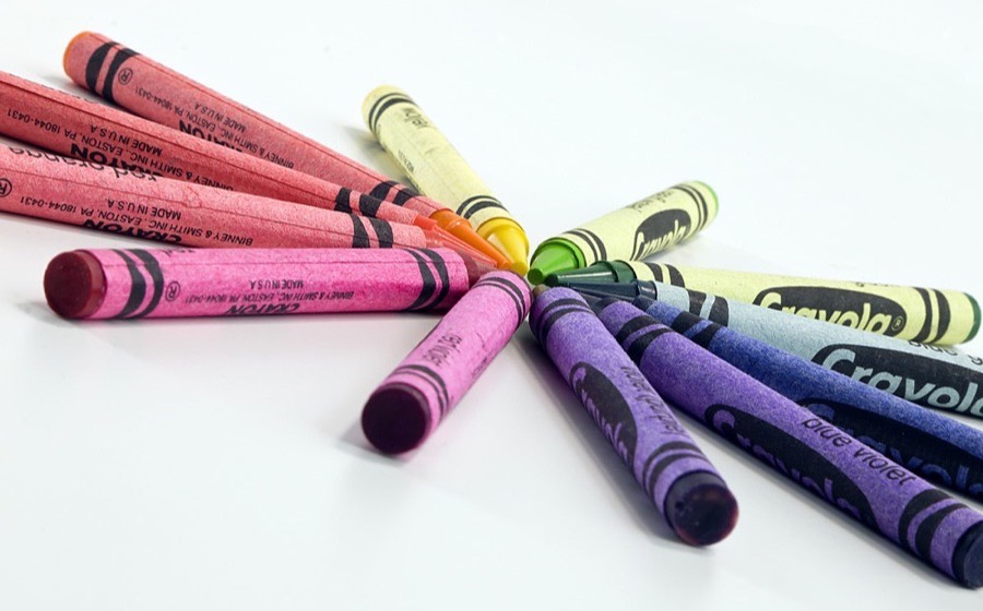 A fan of brightly coloured wax crayons on a white surface.