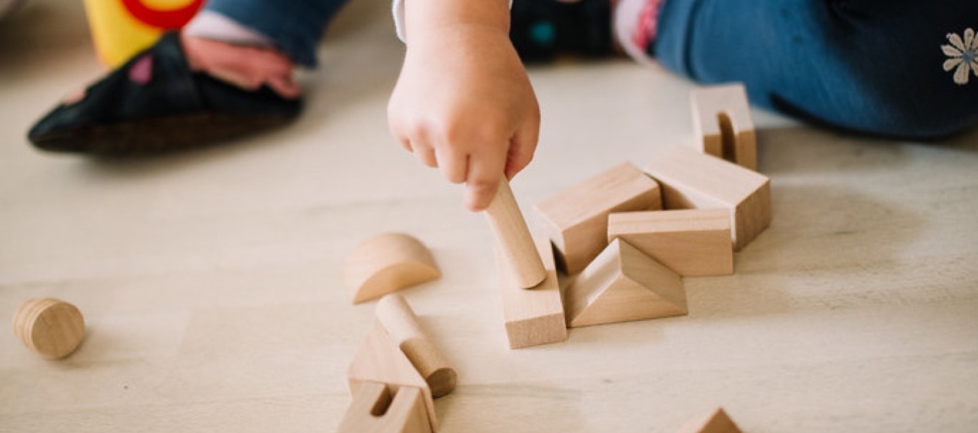 A child's hands arranging plain wooden blocks on a pale floor.