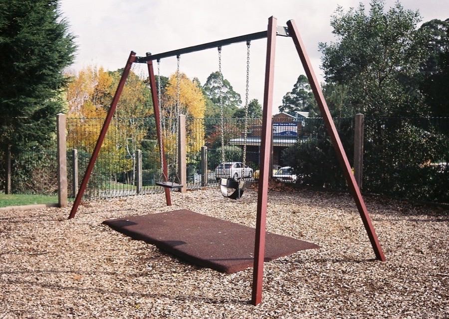 An empty swing set in a suburban playground, ringed by autumn trees.